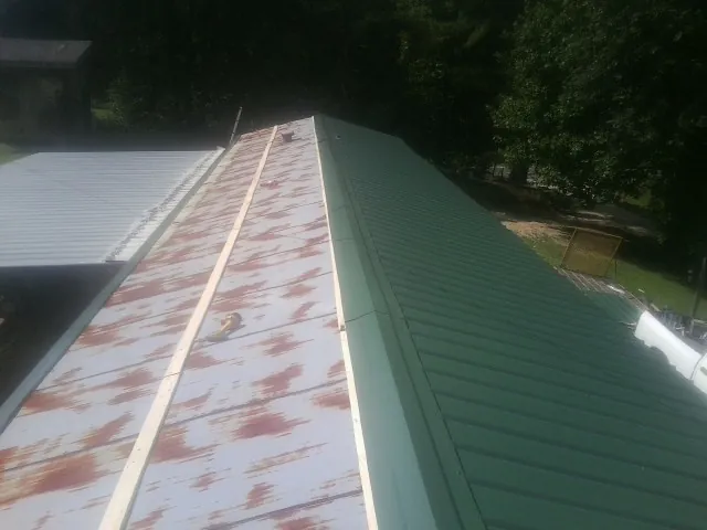 Old rusted panels beside newly installed green metal roofing — Wind Damage Roof Repair by Roofing Brothers in Buena