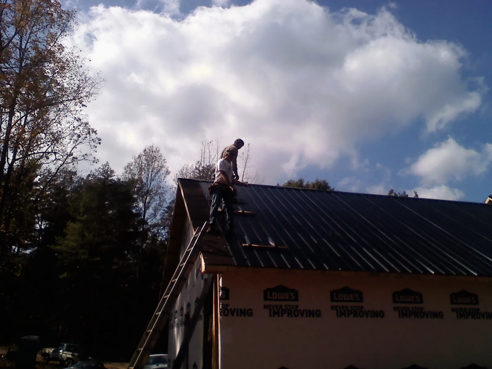 Roofer fastening dark metal panels high against a cloudy sky, from a Roof Inspection job in Buena
