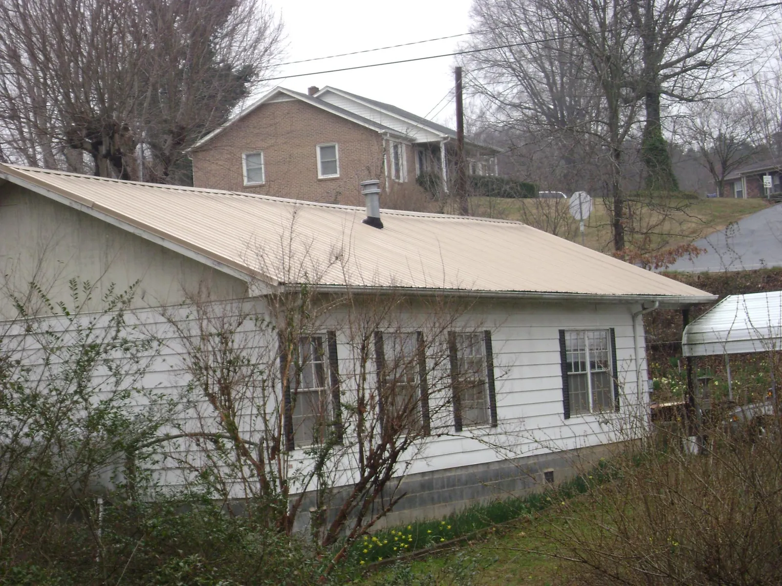 Tan metal roof on a white sided house set into a hillside — Commercial Roofing by Roofing Brothers in Buena